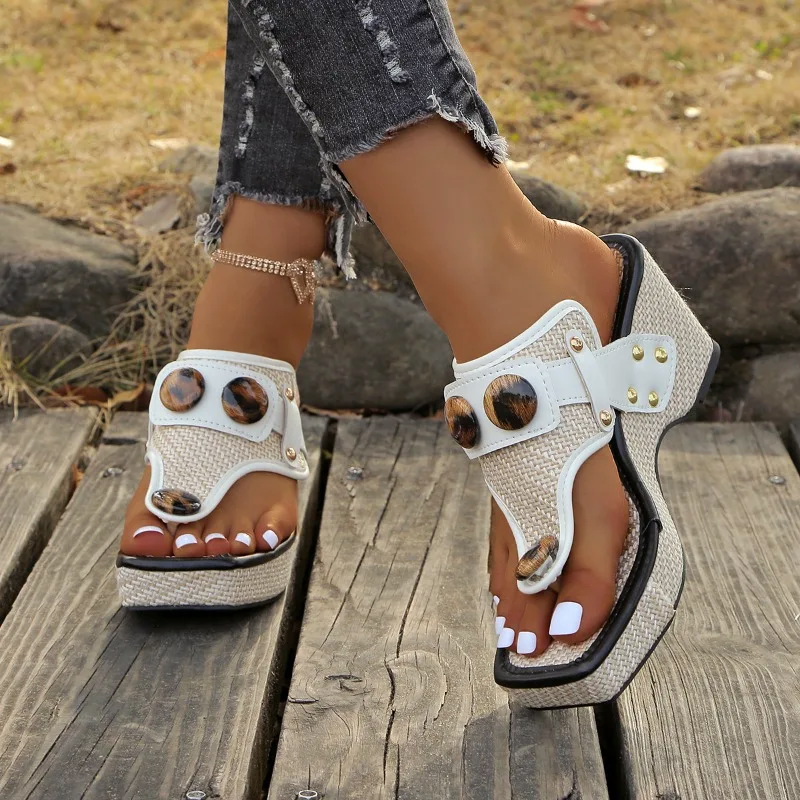 Beige and black strappy wedge sandals worn on wooden planks