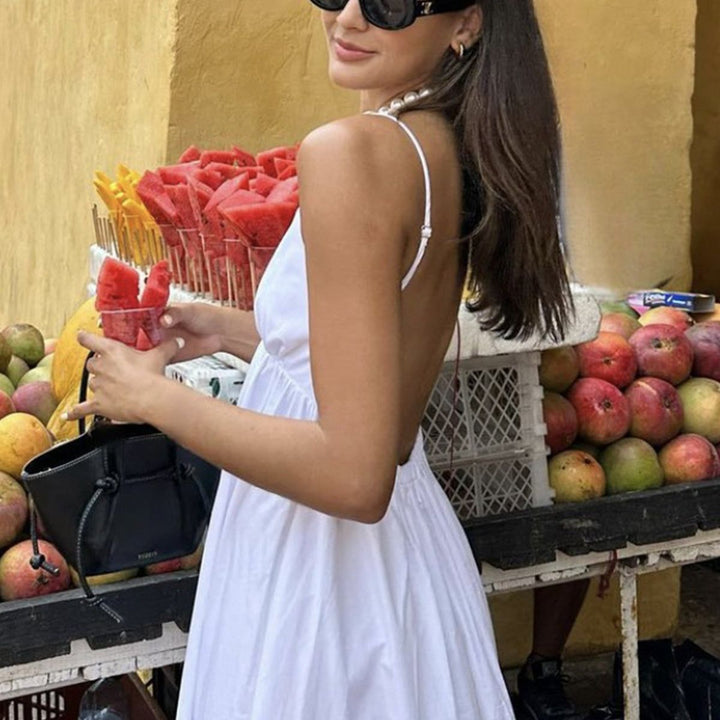 White backless maxi dress styled with sunglasses and handbag for resort wear