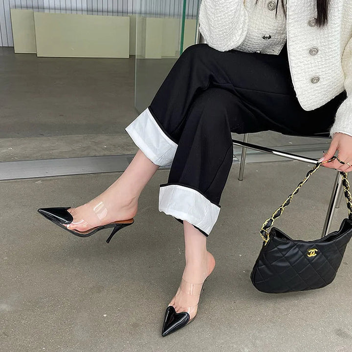 Black patent heart-toe stiletto mules with clear PVC strap crossed over leg open back