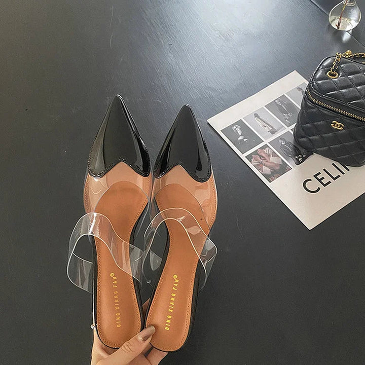 Top-down view of black patent heart-toe stiletto mules with clear PVC strap and branded insole