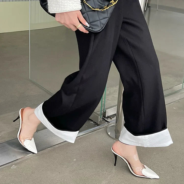 White patent heart-toe stiletto mules with clear PVC strap captured mid-stride