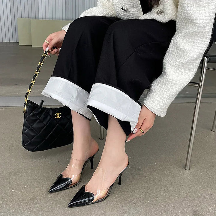 Black patent heart-toe stiletto mules with clear PVC strap worn with wide-leg trousers