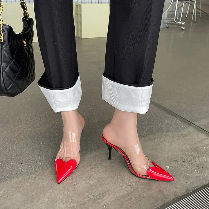 Red patent heart-toe stiletto mules with clear PVC strap close-up on concrete floor