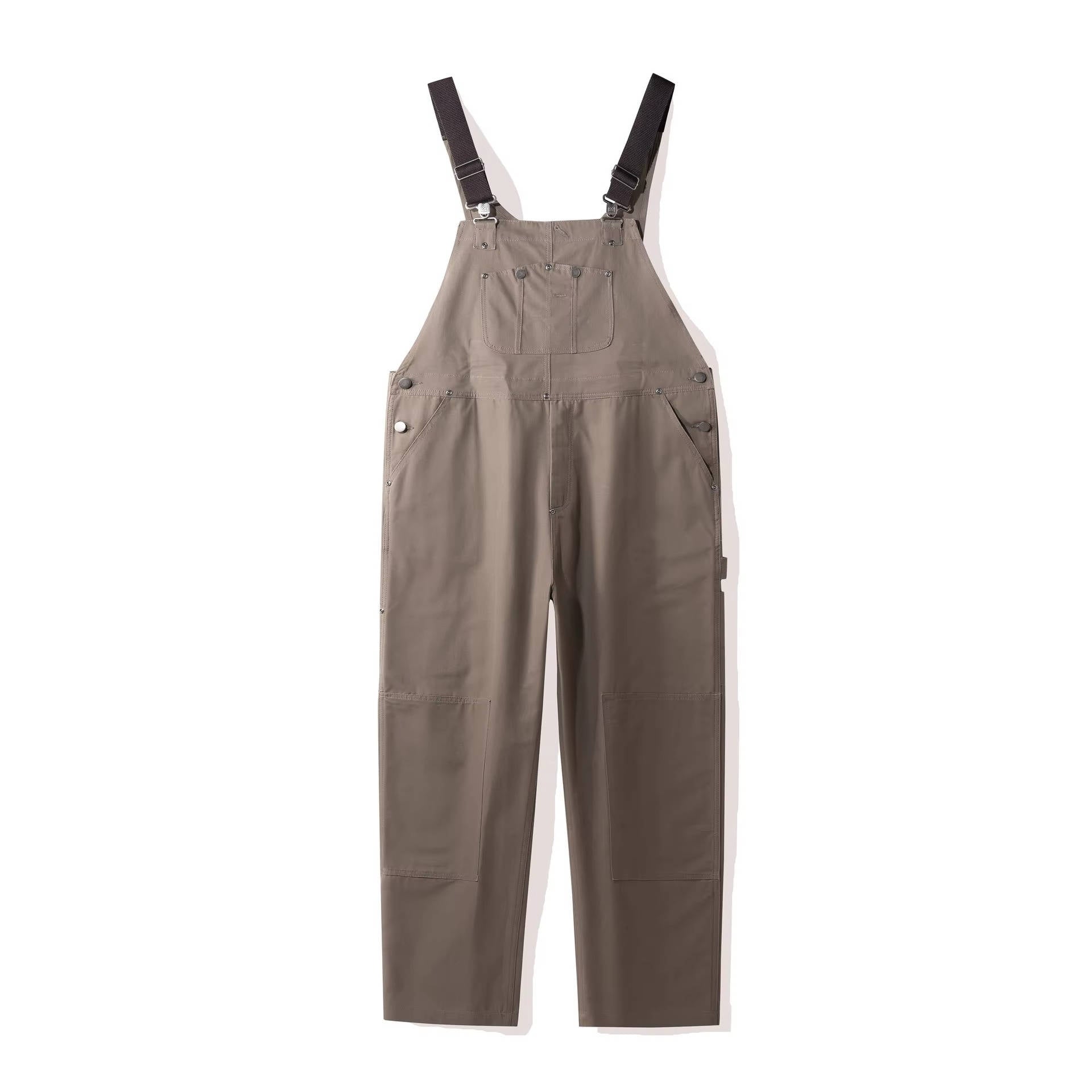 Beige-gray canvas bib overalls flat lay with silver snap buttons and woven texture