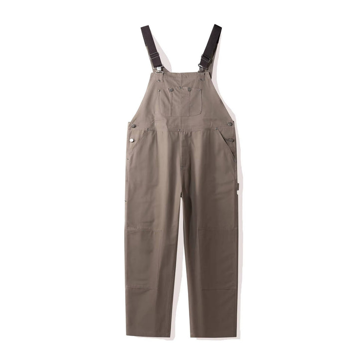 Beige-gray canvas bib overalls flat lay with silver snap buttons and woven texture