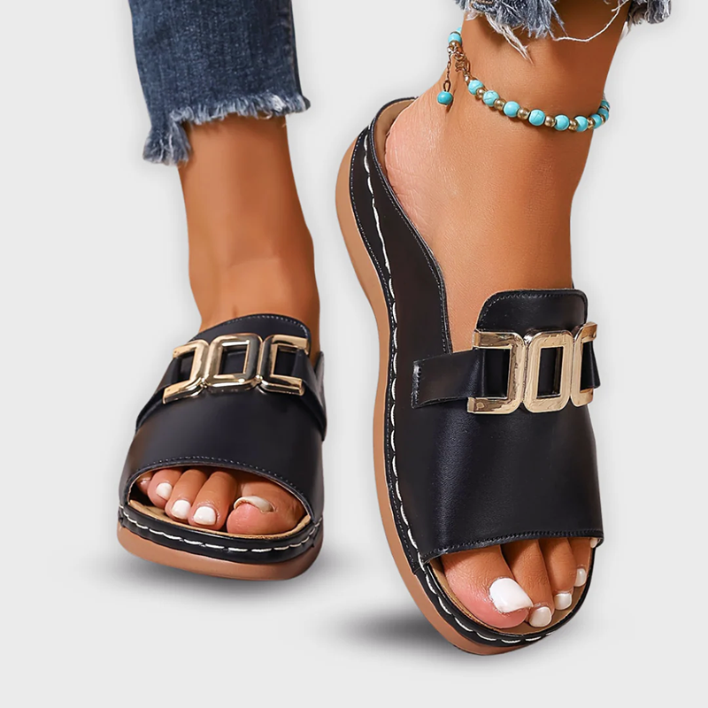 Black faux leather women's backless mule slide sandals with gold buckle shown on feet with jeans